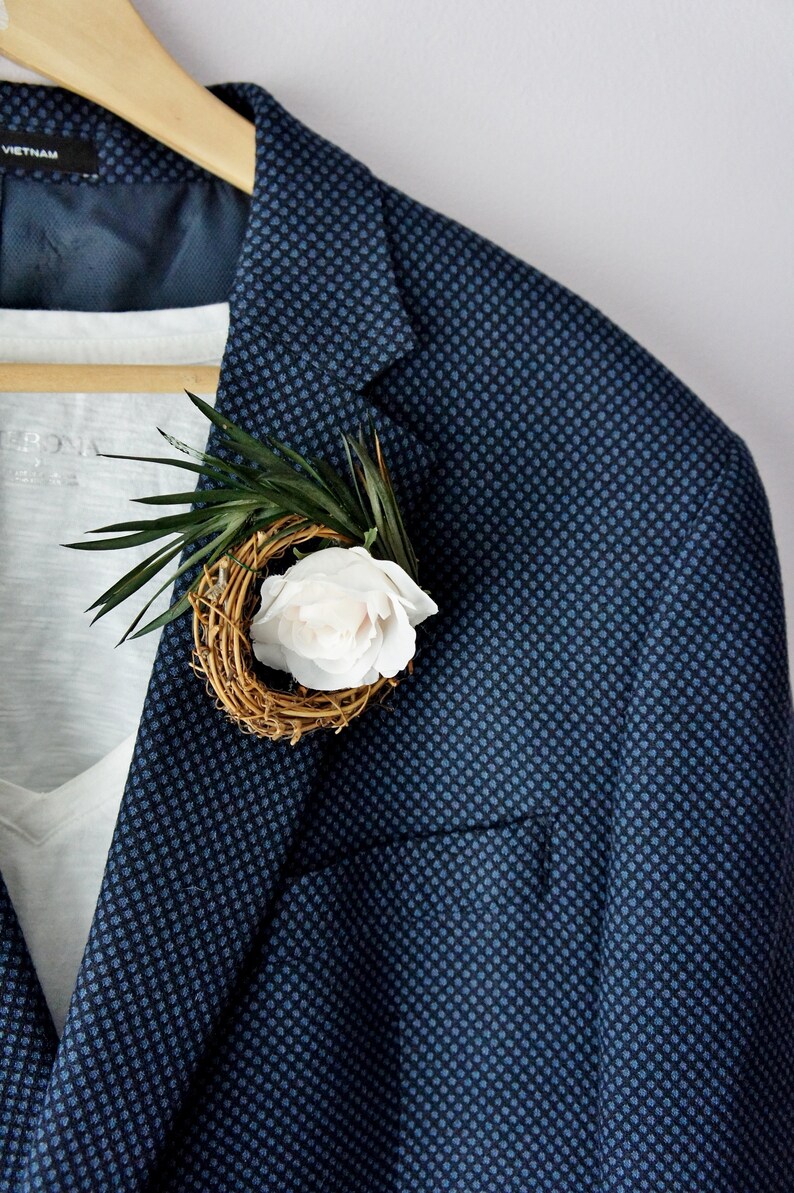 May include: A navy blue blazer with a small white flower and green leaves in a woven nest.