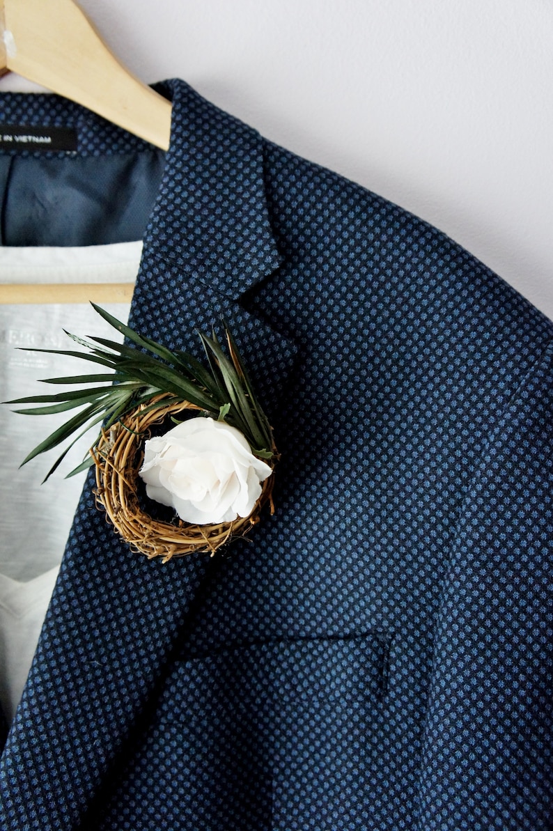 May include: A blue blazer with a small white flower and green leaves in a woven nest.