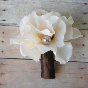 May include: A single white silk flower with a pearl accent, attached to a brown ribbon.
