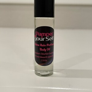 Może przedstawiać: Przezroczysta butelka szklana z czarną zakrętką i etykietą. Etykieta zawiera napis "Pamper your Self" w różowych i czarnych literach. Butelka zawiera perfumowany olejek do ciała China Rain. Składniki są wymienione jako olejek zapachowy China Rain, słodkie migdały i olej jojoba. Butelka zawiera 2,7 fl oz.