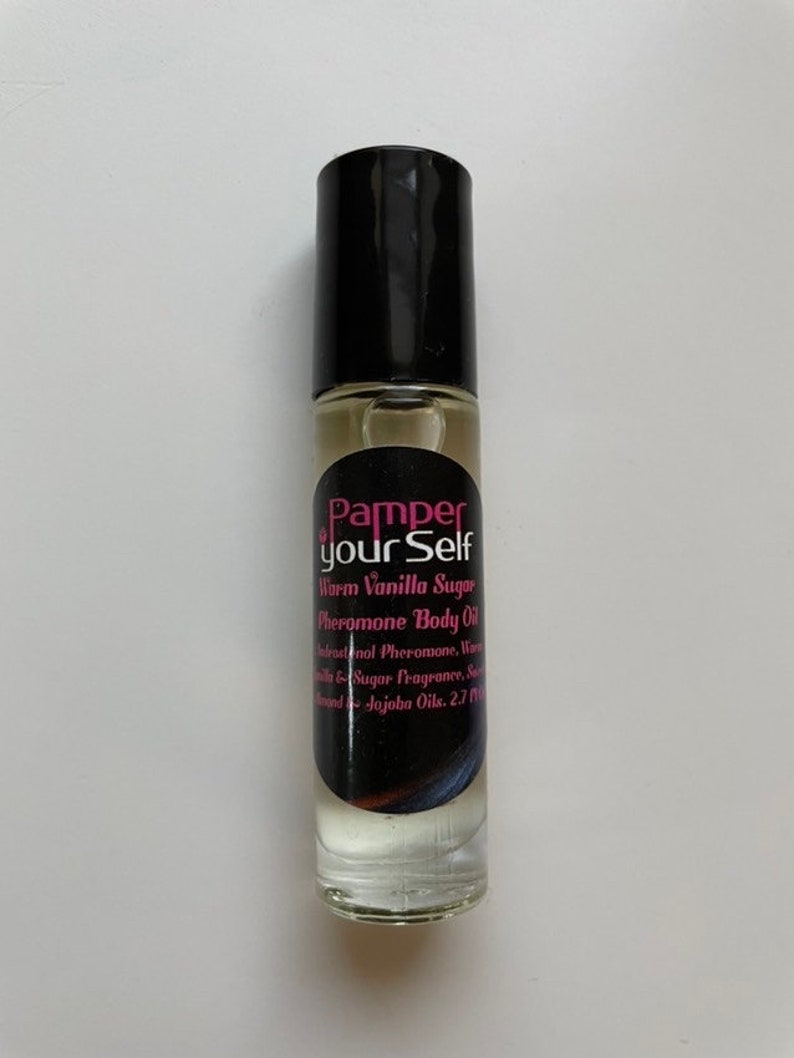 Może przedstawiać: Przezroczysta szklana butelka z kulką z czarną nakrętką. Etykieta głosi "Pamper your Self Warm Vanilla Sugar Pheromone Body Oil". Butelka zawiera jasno zabarwioną ciecz i ma 80 ml.