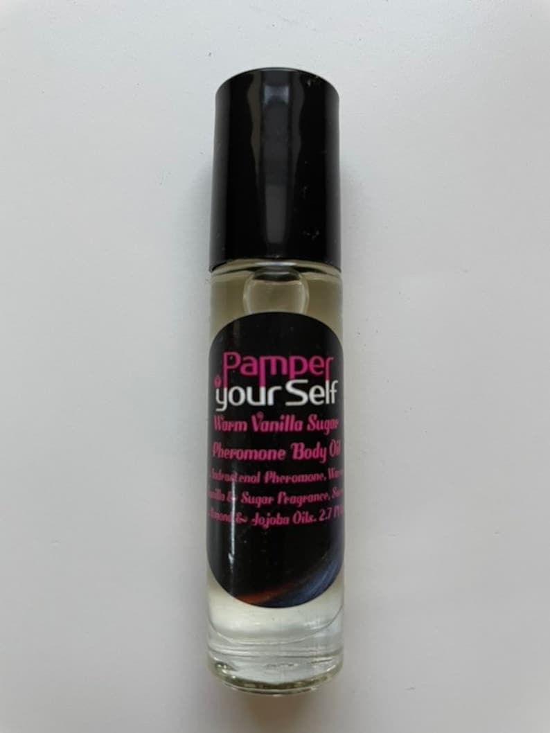 Może przedstawiać: Przezroczysta szklana butelka z kulką z czarną nakrętką. Etykieta głosi "Pamper your Self" i wymienia składniki takie jak Warm Vanilla Sugar Pheromone Body Oil i Jojoba Oils. Butelka zawiera jasno zabarwioną ciecz.