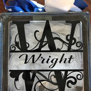 May include: A clear glass block with the name "Wright" in black script, and a large black "W" above and below the name. The block is decorated with white tulle and topped with a blue and white polka dot ribbon and a white ribbon.
