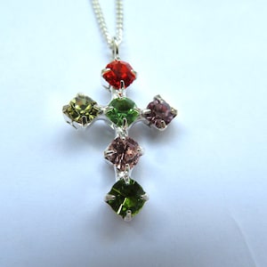 May include: Silver cross pendant with six colorful square-shaped gemstones. The gemstones are red, green, and pink.