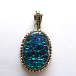 May include: A silver pendant with a blue and green iridescent glass oval inlay. The pendant has a beaded border and a silver bail.