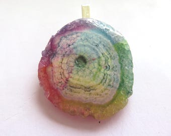 Peut inclure: Un pendentif rond en agate multicolore avec un trou au centre. L'agate présente un arc-en-ciel de couleurs, notamment le rose, le violet, le bleu, le vert et le jaune.