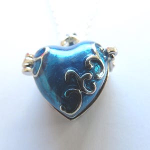 May include: A blue heart-shaped locket pendant with silver filigree details. The locket is open and has a silver chain.