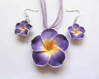 Peut inclure: Un collier et des boucles d'oreilles assortis en forme de fleurs violettes et jaunes. Le collier a un long cordon et les boucles d'oreilles ont des crochets argentés.