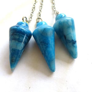Pode incluir: Três pêndulos de cristal de ágata azul com correntes prateadas. Os pêndulos são pontiagudos e têm um padrão azul e branco em espiral.