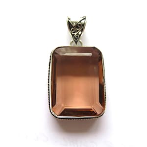 May include: A rectangular pendant with a large, faceted, smoky quartz gemstone. The gemstone is set in a silver-toned metal frame with a decorative bail. The pendant is a neutral color and would complement many outfits.