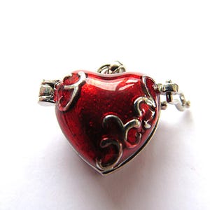 May include: A heart-shaped locket with a glossy red finish and silver filigree detailing. The locket has a hinged opening and a silver clasp. The design is romantic and decorative.