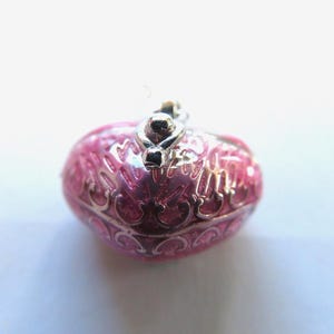 May include: A pink and silver heart-shaped trinket box with an ornate design. The box has a hinged lid and a small silver loop on top.