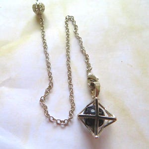 May include: A silver chain with a silver cage pendant containing a black crystal. The cage is shaped like a diamond.