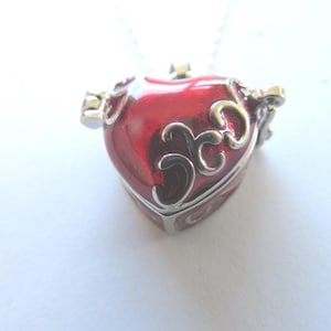 May include: A red heart-shaped locket necklace with a silver chain and ornate silver detailing. The locket has a hinged lid and a small silver charm on the side.