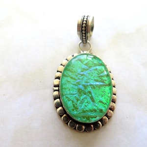 Könnte beinhalten: Ein silberner Anhänger mit einem grünen, irisierenden, ovalen Glascabochon, der in einer Perlenfassung sitzt.