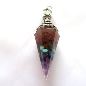 May include: A silver and crystal pendant featuring a clear quartz point and a seven chakra crystal cluster within. The cluster comprises red, orange, yellow, green, blue, indigo, and violet crystals.