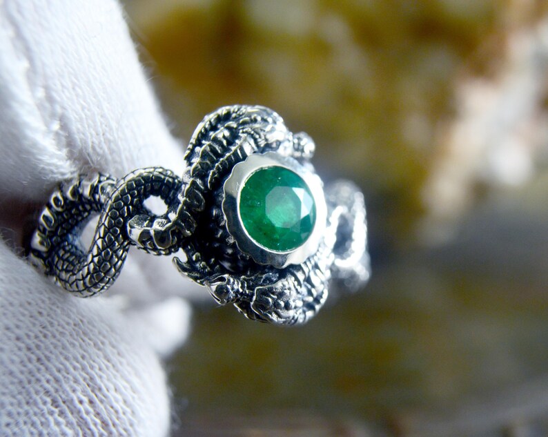 May include: A silver ring with a green gemstone set in a dragon design.