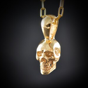 May include: A gold skull pendant necklace. The skull is detailed and has a smooth, shiny finish.