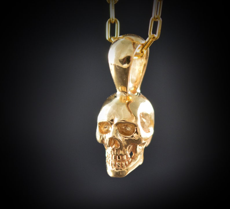 May include: A gold skull pendant necklace. The skull is detailed and has a smooth, shiny finish.