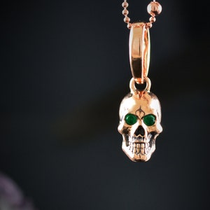 May include: A gold skull pendant necklace with green gemstone eyes. The pendant is on a gold chain.