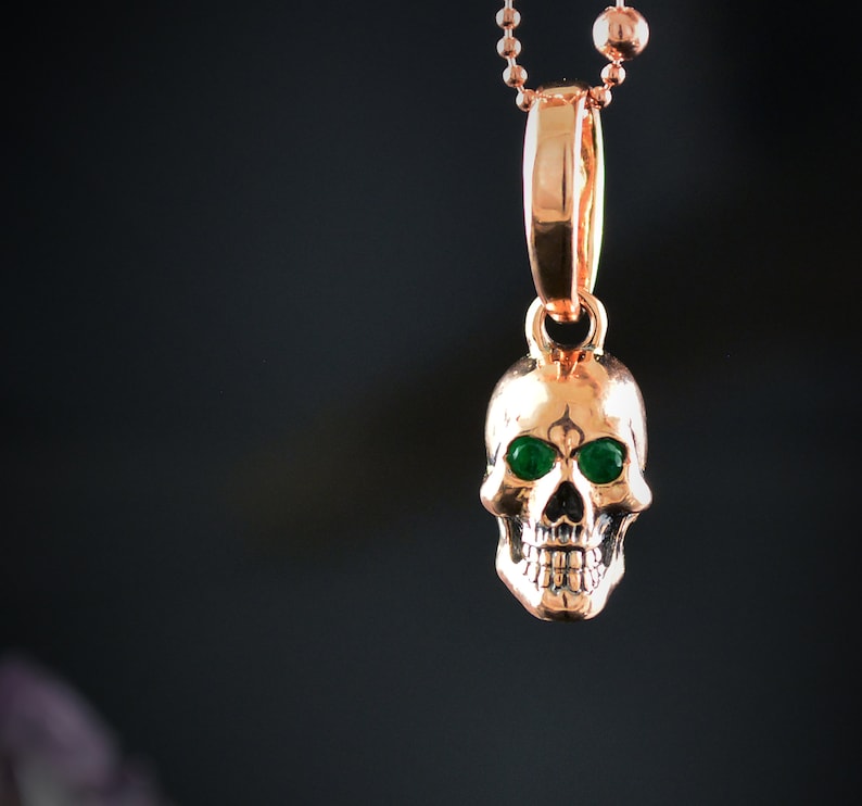 May include: A gold skull pendant necklace with green gemstone eyes. The pendant is on a gold chain.