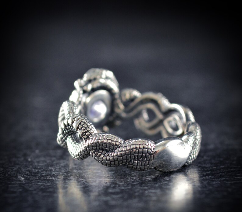 May include: A silver ring with a snake design. The ring is made of intertwined snakes with a textured surface. The ring is a statement piece and would make a great gift.
