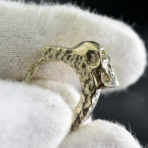 K&ouml;nnte beinhalten: Ein silberner Totenkopfring mit strukturierter Oberfl&auml;che. Der Ring ist an einer Seite offen und der Totenkopf schaut nach rechts.