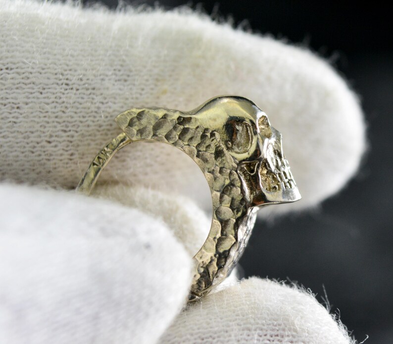 K&ouml;nnte beinhalten: Ein silberner Totenkopfring mit strukturierter Oberfl&auml;che. Der Ring ist an einer Seite offen und der Totenkopf schaut nach rechts.