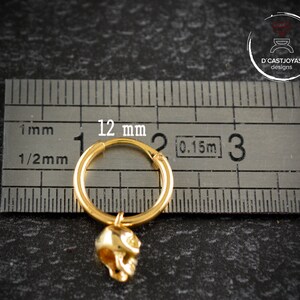 May include: Gold hoop earring with a skull charm. The hoop is 12 mm in diameter. The skull charm is about 1/2 inch long.