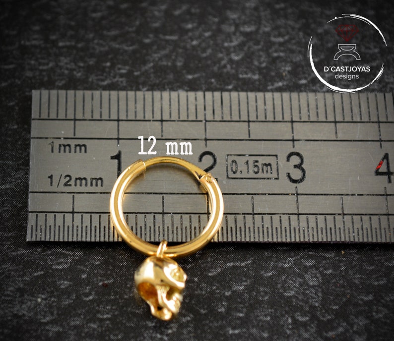 May include: Gold hoop earring with a skull charm. The hoop is 12 mm in diameter. The skull charm is about 1/2 inch long.