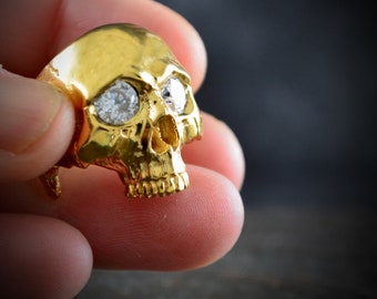 May include: A gold skull ring with two clear diamond-like stones for eyes.