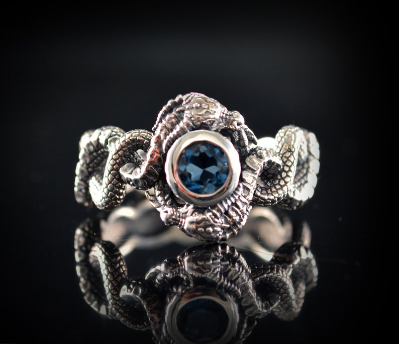 May include: A silver ring with a blue gemstone set in a dragon design.