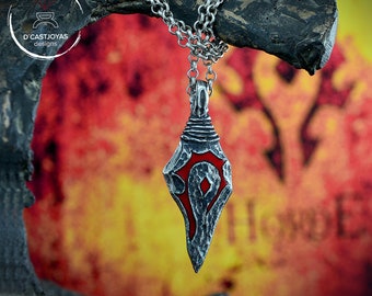 May include: A silver pendant necklace with a red and gray, pointed, teardrop-shaped charm. The charm features a stylized symbol with a diamond shape in the center.