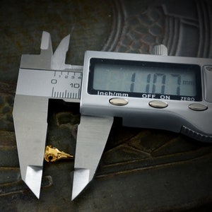 May include: A silver digital caliper measuring a small gold-colored object. The caliper reads 1.07 mm.