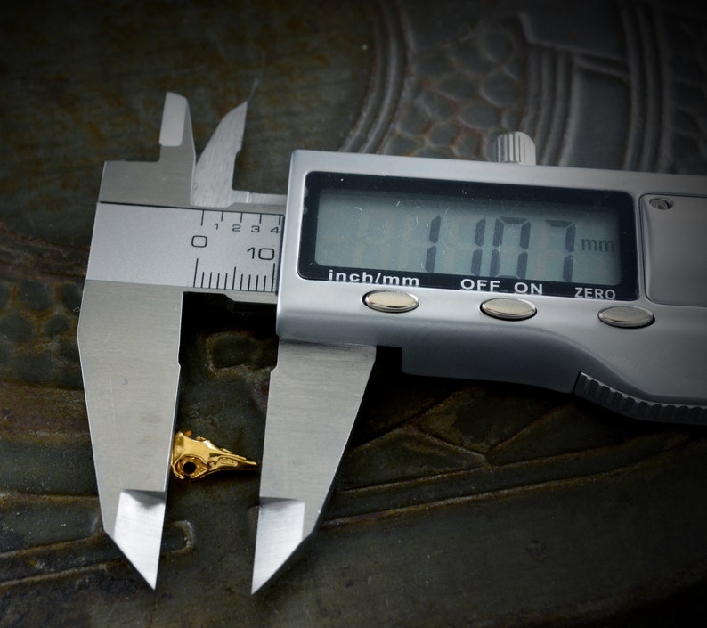 May include: A silver digital caliper measuring a small gold-colored object. The caliper reads 1.07 mm.