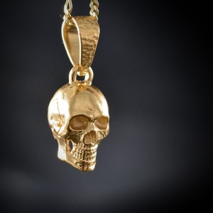 May include: A gold-colored skull pendant necklace. The skull is detailed with eye sockets, a nose, and a mouth.