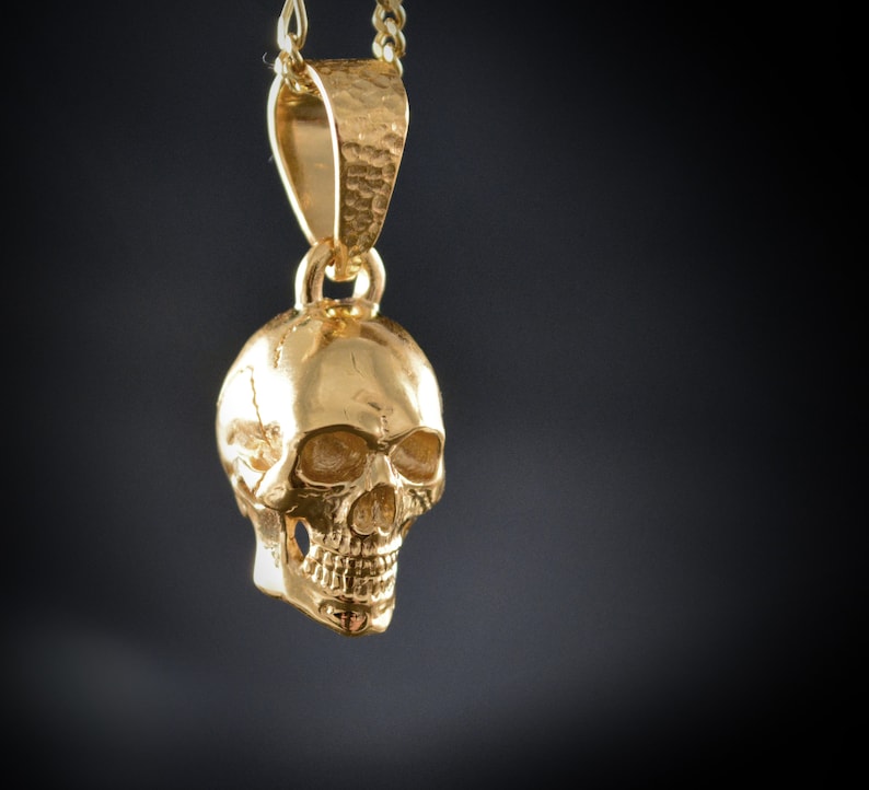 May include: A gold-colored skull pendant necklace. The skull is detailed with eye sockets, a nose, and a mouth.