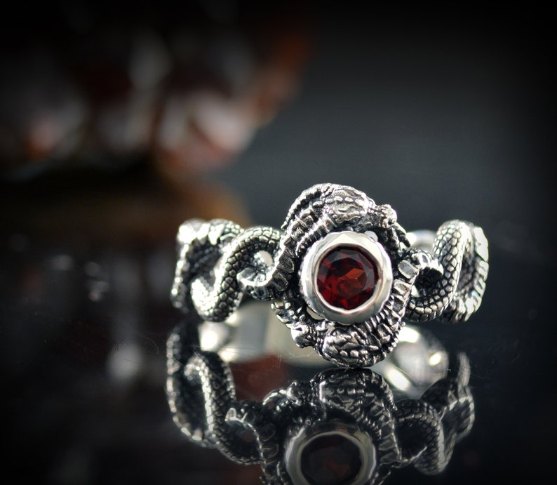 May include: A silver ring with a red gemstone set in a detailed snake design.