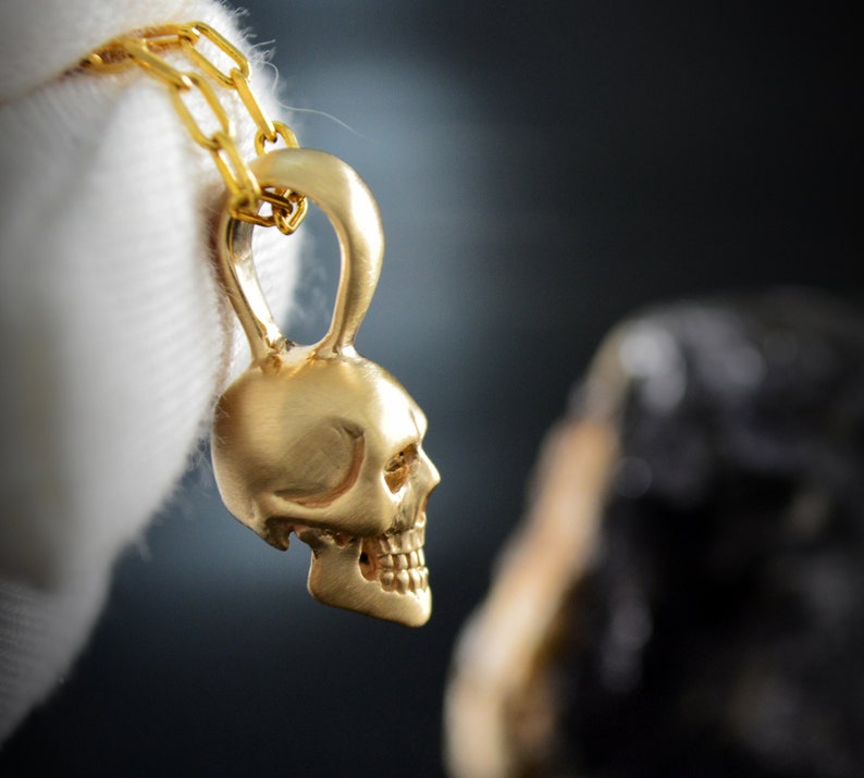 May include: A gold skull pendant necklace with a chain. The skull has a detailed design and is a popular style of jewelry.