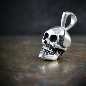 Pu&ograve; includere: Un ciondolo a forma di teschio in argento con un anello per una catena. Il teschio &egrave; dettagliato con orbite, un naso e denti.