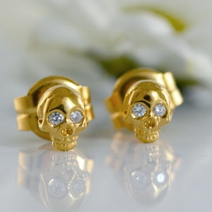Puede incluir: Un par de pendientes de calavera de oro con detalles de diamantes. Los pendientes son pequeños y delicados, y serían un gran regalo para alguien que ama las joyas únicas.