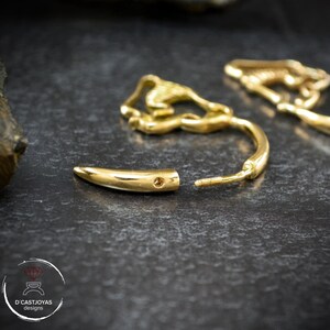 Op de afbeelding: Een paar gouden creolen met een uniek ontwerp. De ene oorring is een eenvoudige creool, terwijl de andere een gouden tandvormige hanger heeft.