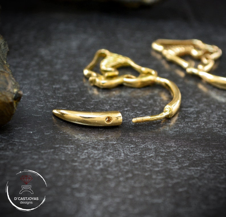 Op de afbeelding: Een paar gouden creolen met een uniek ontwerp. De ene oorring is een eenvoudige creool, terwijl de andere een gouden tandvormige hanger heeft.