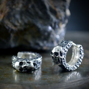K&ouml;nnte beinhalten: Zwei silberne Totenkopf-Creolen mit strukturierter Oberfl&auml;che. Die Ohrringe sind aus Sterlingsilber gefertigt und haben ein Totenkopf-Design.