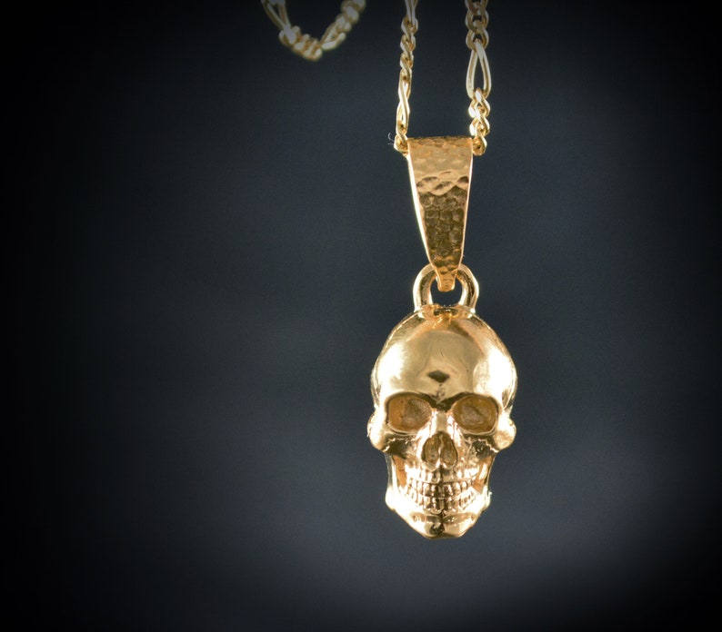 May include: A gold skull pendant necklace with a delicate chain. The skull is detailed with eye sockets, a nose, and a mouth.