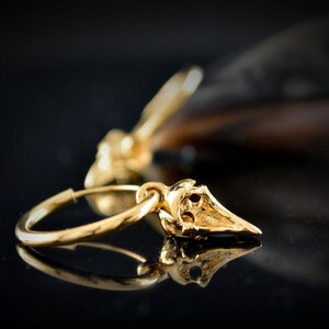 May include: Gold hoop earrings with a small, detailed, gold bird charm hanging from each hoop.