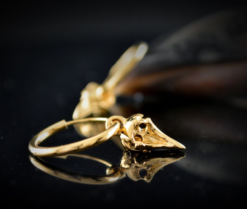 May include: Gold hoop earrings with a small, detailed, gold bird charm hanging from each hoop.