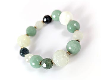 May include: A beaded bracelet featuring a mix of green, white, and black gemstone beads. The bracelet includes round and faceted beads in various sizes, strung together with gold-colored accents. The gemstones have a polished finish.