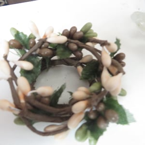 May include: A brown twig wreath with white and brown berries and green leaves. The wreath is about 6 inches in diameter.