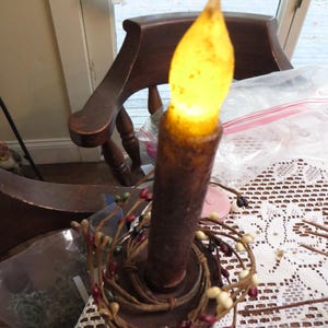 May include: A brown candle with a yellow flame, decorated with a brown and white berry garland.